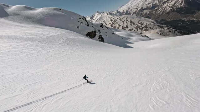 FPV sports drone shot man skier freeride downhill extreme speed movement recreation at winter mountain landscape. Aerial view ski sportsman riding on snow cliff slope frozen seasonal outdoor hobby 4k