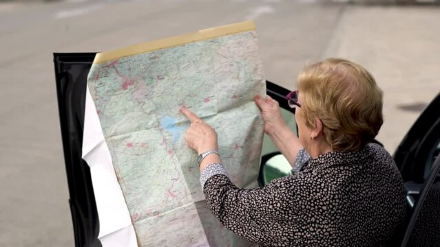 Senior woman with a map outside a car