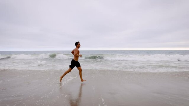 Athletic man jogging at the beach in Southern California. Slow Motion.