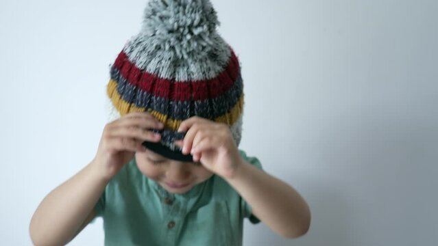One cute little boy wearing beanie peeking out. Child face covered with knit wool accessory