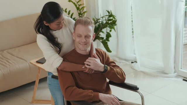 Young Asian woman hugging her beloved man in wheelchair from behind