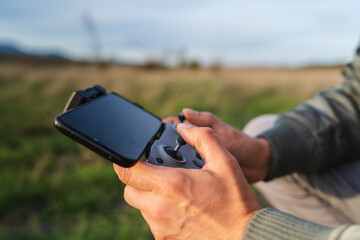 A man is operating a drone with a controller outside during the day