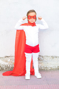 Little girl in superhero costume showing muscles against wall