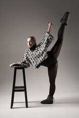 Ballet dancer woman black dress on gray background, Ballerina posing and showing her flexibility on gray background in studio with chair. Text on sweater DREAMS OF
