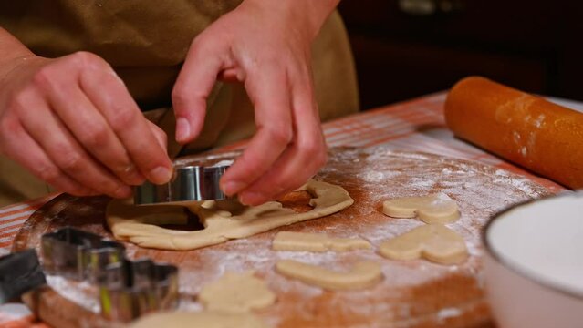 Close-up pastry chef using cookie cutters, carving angel wings from gingerbread dough while making homemade festive Christmas pastries. Baking concept. Culinary