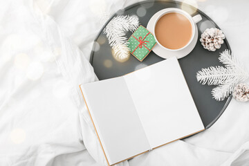Tray with cup of coffee, Christmas cookie, decor and blank book on bed