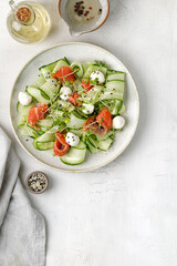 Diet healthy salad with salmon, sliced cucumbers, mozzarella cheese, microgreens on grey ceramic plate and stone background.