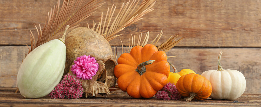 Beautiful composition with Halloween pumpkins, flowers and human scull on wooden background