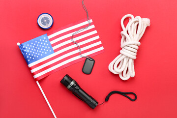 National flag of USA, military tag, flashlight, compass and rope on red background