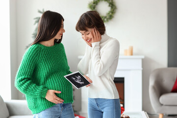 Young pregnant woman with sonogram image and her wife at home