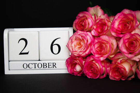  October 26 wooden calendar, white on a black background, pink roses lie nearby.Postcard with copy space. The concept of a holiday, congratulation, invitation, party, announcement, vacation,promotion.