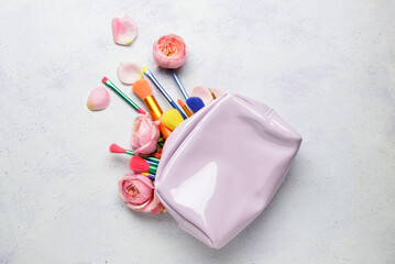 Makeup bag with different brushes and roses on light background