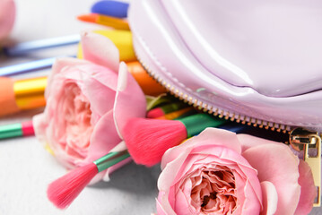 Makeup bag with different brushes and roses on light background, closeup