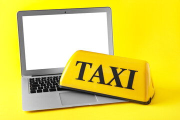Taxi roof sign and modern laptop on yellow background