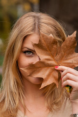 Portrait of a young woman with long blonde hair hiding behind a leaf