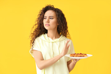 Young African-American woman refusing from pastry on yellow background. Diet concept