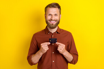 Portrait of positive person arms hold debit plastic card toothy smile isolated on yellow color...