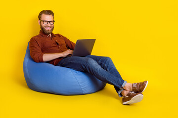 Full body photo of positive person sit comfy bag use wireless netbook isolated on yellow color background