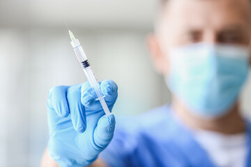 Male doctor in medical mask with syringe at hospital, closeup