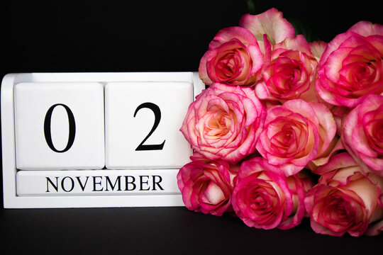 November 2 wooden calendar, white on a black background, pink roses lie nearby.Postcard with copy space. The concept of a holiday, congratulation, invitation, party, announcement, vacation,promotion.