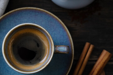 Blue coffee cup with saucer and cinnamon sticks on wooden background.