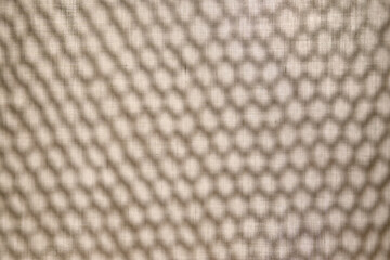 Abstract background. The shadow from the mesh in the form of honeycombs on the fabric.