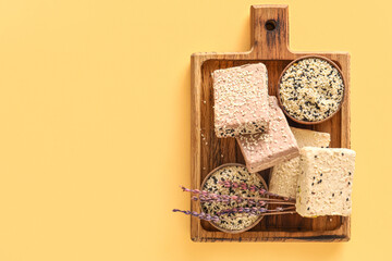 Wooden board with bowls of sesame seeds and sweet halva on color background