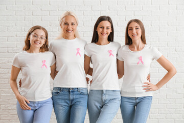 Obraz premium Beautiful women with pink awareness ribbons hugging on white brick background. Breast cancer concept