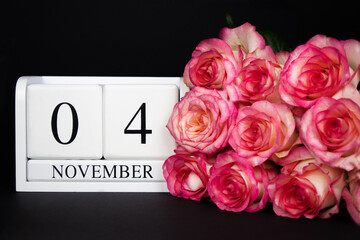 November 4 wooden calendar, white on a black background, pink roses lie nearby. Postcard with copy space. The concept of a holiday, congratulation, invitation, party, announcement, vacation,promotion.