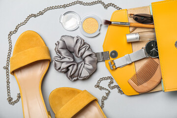 Stylish female shoes and opened bag with accessories on grey background