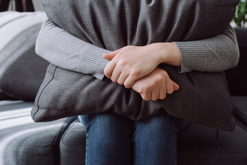 Close up of unhappy lonely depressed young female, upset anxiety woman sitting on couch and hiding face on grey pillow, depression concept. Girl going through emotional crisis after abuse abortion