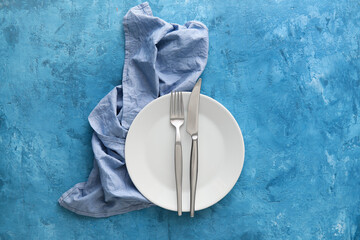 Simple table setting with cutlery in plate and napkin on blue background