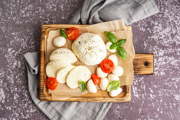 Wooden board with delicious mozzarella cheese, basil and tomatoes on grunge background