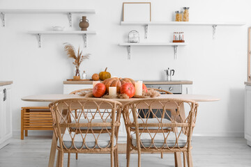 Dining table with pumpkins, pampas grass and burning candles in light kitchen