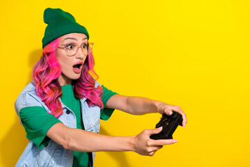 Portrait of excited gorgeous girl curly hairdo wear green t-shirt look empty space play video game isolated on yellow color background © deagreez