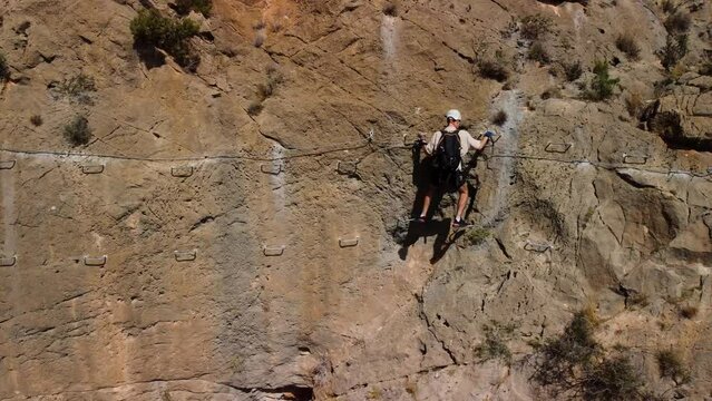 Man climbs a via ferrata traverse sideways, from left to right, equipped with climbing equipment