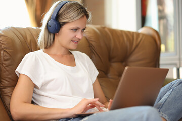 Young woman in headphones sitting on sofa and working on laptop