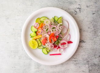 Fresh salad with onion, cucumber, carrot, lemon and tomato served in a plate isolated on background...