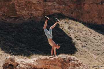 a man of athletic build performing a handstand on a large rock in a canyon gorge, adhering to a healthy lifestyle of proper nutrition - Powered by Adobe