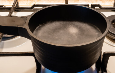 Blurred motion image of boiling water in black metal pot on gas stove close-up