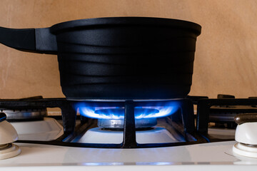 Black metal pot on gas stove close-up on blurred kitchen background. Side view