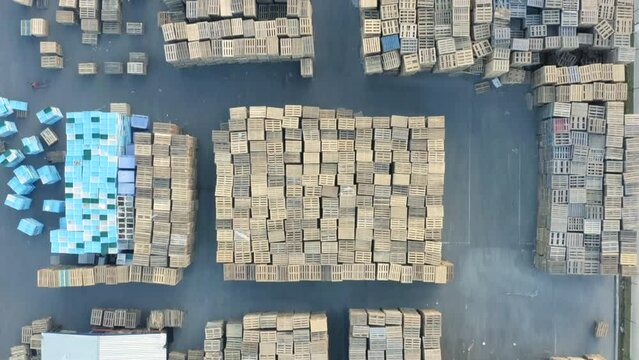 Aerial top view of a storage yard or open storage warehouse of wood pallets with working forklifts 