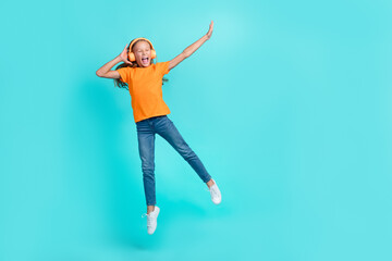Fototapeta na wymiar Full length photo of cheerful positive little child dressed orange t-shirt earphones jumping high empty space isolated teal color background