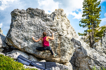 Naklejka na ściany i meble Sporty woman climbs on boulder problem in the afternoon. Falzarego pass, Dolomites, South Tirol, Italy, Europe.