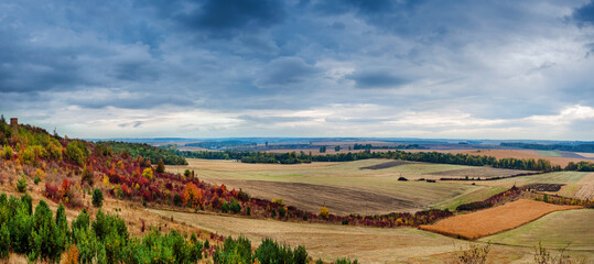 panoramic landscape of farmland in autumn with colorful trees and dramatic sky, top view.
