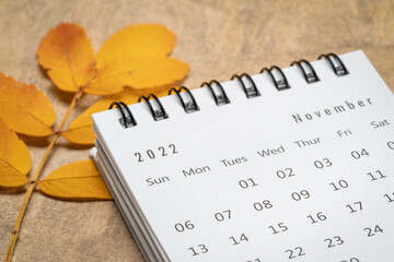 November 2022 - small spiral desktop calendar against textured handmade paper, low angle macro...