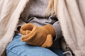 Fototapeta na wymiar Frozen. A young woman sits on the floor in an apartment in a warm sweater, plaid and mittens and is shivering from the cold. Problems with the heating system in the cold season of the year
