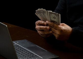 Computer and hands of a man wearing a black shirt, sitting on a chair and a table, is a thief,...