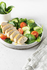 Healthy green salad with chicken breast and fresh vegetables spinach, cucumber and tomato on white bacground with linen napkin. Healthy lunch menu. Keto diet, detox food concept with text space
