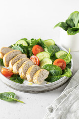 Roasted chicken fillet and fresh vegetable salad of spinach, cucumber and tomato on white bacground with linen napkin. Healthy lunch menu. Keto diet, detox food concept